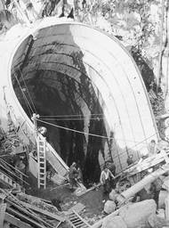 Budoucí šachta nákladního výtahu do 160 metrů hluboko uložené podzemní strojovny vodní elektrárny. V březnu 1954 byly zahájeny práce na šikmém tunelu. Podobný projekt byl v té době v Evropě výjimečný, protože prorážení šachty pod úhlem 45 stupňů bylo technicky velmi náročné. Pro zpevnění skály byly použity dřevěné výztuhy nazývané "kapny" a před každým odstřelem bylo nutné přemístit veškeré vybavení, aby nedošlo k jeho poškození. Pro zabránění zatopení šikmého tunelu byla neustále v provozu vzduchová čerpadla, která odčerpávala vodu.