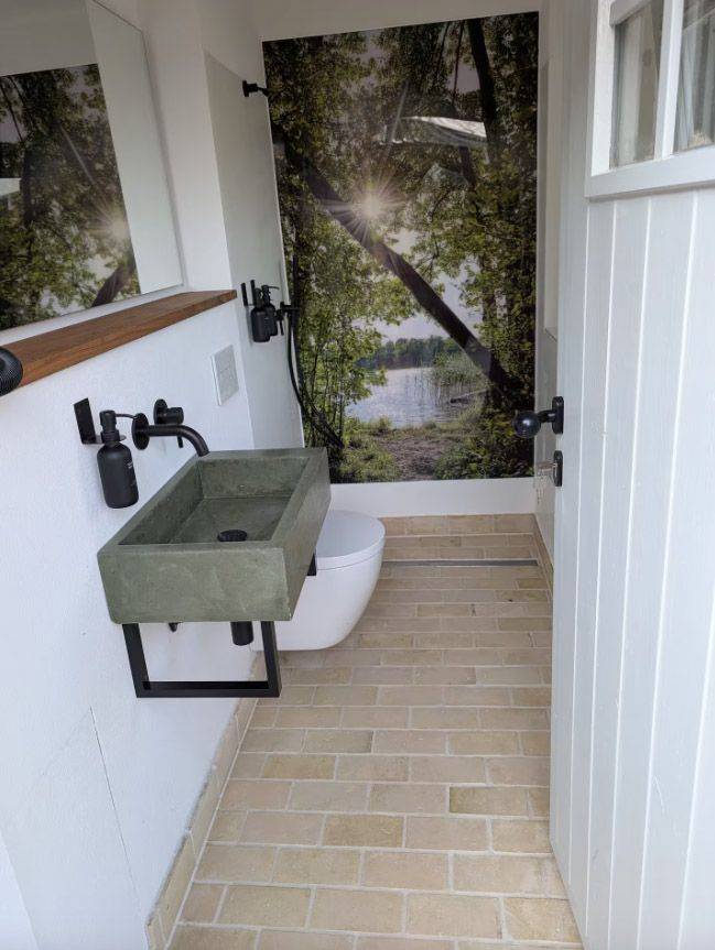 V bývalé trafostanici se nachází kompaktní koupelna se sprchovým koutem, podlahové vytápění, sezení, které má návštěvníky spojit s okolím, a rozkládací pohovka.