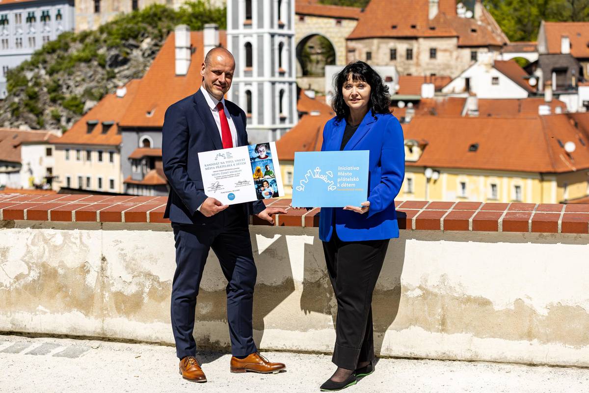 Český Krumlov se stal historicky prvním městem v České republice, které převzalo kandidátské logo iniciativy UNICEF „Města přátelská k dětem“. Slavnostní akt předání loga nebyl jen symbolickým oceněním dosavadního úsilí města o vytvoření prostředí vstřícného k dětem, ale především závazkem do budoucna – naslouchat dětem, podporovat jejich aktivní zapojení do veřejného života a společně budovat město, kde se každý mladý člověk cítí respektován. Předání certifikátu proběhlo v kině Luna poslední dubnový den, který byl plný inspirace, sdílení zkušeností a plánování dalších kroků. Součástí byly diskuze s mladými řečníky z nejrůznějších oborů, kteří ukázali, že i děti a mládež mohou mít reálný dopad na dění kolem sebe. Se svým příspěvkem o tom, že vzdělávání může být živé, zábavné a dostupné všem, vystoupil například Robin Řežábek, českobudějovický pedagog a 4fun streamer, kterého sledují tisíce žáků a studentů online.  Akce v kině se zúčastnili žáci základních škol, členové školních parlamentů i Parlamentu dětí a mládeže Český Krumlov. „Jde o završení šestiletého úsilí a titul je jen třešnička na dortu. To důležité je, že měníme přístup – že děti dostávají prostor, kde se mohou vyjádřit, a my jim nasloucháme,“ říká starosta Alexandr Nogrády. Český Krumlov se v rámci iniciativy „Město přátelské k dětem“ zavázalo k celé řadě konkrétních kroků, které podporují aktivní zapojení dětí a mládeže do veřejného života. Klíčovou roli v tomto procesu zastává Parlament dětí a mládeže, který disponuje participativním rozpočtem – tedy prostředky, o jejichž využití rozhodují přímo děti. Dalším počinem je např. program, který umožní mladým lidem stínovat zástupce samosprávy, získat přímou zkušenost s rozhodovacími procesy a lépe porozumět fungování města. Participace dětí je podporována už na úrovni škol prostřednictvím školních parlamentů, které se stávají místem pro první demokratické zkušenosti. „V projektu Město přátelské k dětem jde o víc než jen o zdravé a bezpečné prostředí. Jde o férovost, o skutečné naslouchání dětem. Často se o dětech mluví jako o budoucnosti, ale ony s námi žijí tady a teď. Vnímat je jako plnohodnotné členy společnosti znamená změnit pohled nás všech,“ uvedla Pavla Gomba, výkonná ředitelka UNICEF ČR. Na počátku procesu, kdy Český Krumlov začal o titul usilovat, proběhl rozsáhlý průzkum mezi dětmi a mládeží, který ukázal, že právě vyšší zapojení do rozhodovacích procesů je tím, co si děti přejí nejvíce. Na základě těchto zjištění si město v rámci svého akčního plánu vybralo participaci dětí a mládeže jako klíčovou oblast, ve které se chce dále rozvíjet. Krátce nato vznikl například Parlament dětí a mládeže Český Krumlov, který plní důležitou roli při prosazování hlasu mladých lidí v rozhodování o dění ve městě.