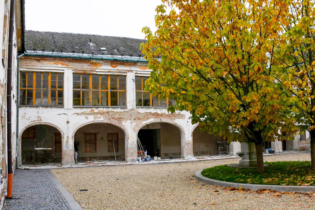 Je to místo, které začíná čím dál tím víc žít…   Závěrečná fáze úprav nádvoří jindřichovského zámku byla s mírným zpožděním úspěšně dokončena. Nově zpevněná plocha orámovaná okapovými chodníky a srovnaná bílým oblázkovým štěrkem dodala prostoru svěží a důstojný vzhled, který harmonicky navazuje na historický charakter místa. Přestože se zčásti nepodařilo dodržet původní harmonogram prací, což se u rekonstrukcí historických objektů může stát, výsledek je už nyní pozoruhodný.  Zářivá plocha nádvoří nyní kontrastuje s fasádou, která historicky nese stopy povětrnostních vlivů i nedávných technických zásahů, zejména v souvislosti s přípravnými elektroinstalačními pracemi a její celková oprava je plánována v dalších etapách stavebních prací. Zmíněný nedostatek však neubírá nic na celkovém pozitivním dojmu z revitalizovaného prostoru, kde v centrální části vynikají tři chráněné stromy, jež byly v průběhu stavby zabezpečeny proti poškození a zachovaly si svůj dřívější svěží a přirozený vzhled.    Co nevidět bude nádvoří plně připravené pro konání kulturních a společenských akcí. Ambitová chodba nabídne zázemí i v případě nepříznivého počasí a nově upravený prostor přispěje nejen k místnímu komunitnímu životu, ale i k rozvoji mezinárodní spolupráce — zejména s obyvateli polského Prudnického Powiatu.  V současné době vrcholí závěrečné zednické práce v ambitové chodbě, která tvoří důležitou součást celkového prostoru nádvoří. Její obnova nejen esteticky sjednotí vstupní část do nádvoří, ale zároveň vytvoří chráněné prostředí pro návštěvníky za nepříznivého počasí.  S ohledem na poválečnou historii zámku a neodborné stavební zásahy do jeho architektonické podoby představuje současná etapa rekonstrukce významný krok směrem k oživení jeho využití. Jindřichovský zámek se tak postupně proměňuje v kulturní a společenské centrum, na které mohou být obyvatelé Jindřichova i patrioti z celého regionu oprávněně hrdí. Jak poznamenal starosta Martin Korduliak: „Je to místo, které začíná čím dál tím víc žít.“