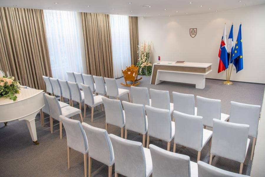 Obradná sieň mesta Trenčianske Teplice je miestom, kde sa odohrávajú dôležité životné okamihy našich obyvateľov – občianske slávnosti, sobáše, jubileá, ale aj prijatia významných hostí. Práve preto je dôležité, aby tento priestor pôsobil dôstojne, reprezentatívne a zároveň príjemne. V uplynulom období prešla obradná sieň viacerými úpravami, ktorých cieľom bolo skvalitniť jej celkový vzhľad a atmosféru. Realizované boli estetické úpravy – výmena nábytku a závesov, ako aj kompletné vymaľovanie miestnosti. Výsledkom je modernejší, svetlejší a čistejší priestor, ktorý dôstojne slúži obyvateľom mesta i jeho hosťom. S obradnou sieňou je neodmysliteľne spätá činnosť Zboru pre občianske záležitosti (ZPOZ) pri Mestskom zastupiteľstve v Trenčianskych Tepliciach. Tento zbor už desaťročia významne prispieva k posilňovaniu ľudskej spolupatričnosti a kultúrnej úrovne spoločenského života v meste. Hoci po roku 1989 činnosť ZPOZ v mnohých regiónoch zanikla a bola označovaná za prežitok minulosti, v Trenčianskych Tepliciach zbor dodnes úspešne funguje. Jeho predsedníčkou je v súčasnosti poslankyňa Mestského zastupiteľstva Daniela Rybanská. Za viac ako polstoročie aktívnej činnosti sa ZPOZ vypracoval medzi najlepšie zbory v kraji. Jeho členovia dôsledne dbajú na to, aby sa občianske obrady a slávnosti konali na vysokej spoločenskej a kultúrnej úrovni. ZPOZ sa venuje najmä tradičným obradom, medzi ktoré patrí uvítanie detí do života, občianske sobáše, životné jubileá, rozlúčka s deviatakmi či občianske pohreby. Okrem toho sa podieľa aj na množstve ďalších podujatí, bez ktorých si už spoločenský život mesta len ťažko vieme predstaviť – oslavy Dňa učiteľov, Mesiaca úcty k starším, stretnutia s jubilantmi, odovzdávanie Ceny Karla Čapka a rôznych ocenení, ako aj slávnostné prijatia vzácnych hostí primátorkou mesta. Medzi hostí, ktorí sa zapísali do pamätnej knihy mesta, patrí napríklad japonský veľvyslanec, predstavitelia amerického veľvyslanectva pri príležitosti Dňa veteránov, ako aj ďalšie zahraničné delegácie a významné osobnosti. Na príprave a realizácii obradov sa podieľajú primátorka mesta, poslanci mestského zastupiteľstva, predsedníčka ZPOZ, matrikár, recitátori, speváci a hudobníci. ZPOZ úzko spolupracuje aj so základnou a materskou školou, ktoré pripravujú deti na vystúpenia pri jednotlivých podujatiach. Vysokú kvalitu obradov opakovane ocenili aj odborné komisie na okresných, regionálnych i celoslovenských prehliadkach zborov. Aj prostredníctvom činnosti ZPOZ a starostlivosti o obradnú sieň Mesto Trenčianske Teplice potvrdzuje, že mu záleží na dôstojných životných okamihoch svojich občanov.