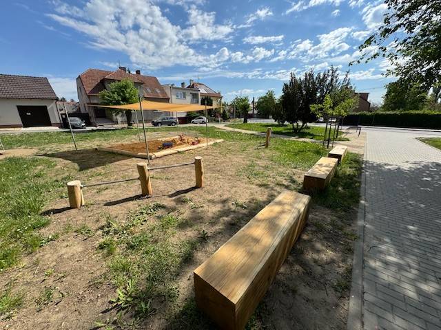 Park pod sokolovnou se postupně proměňuje v prostor, který bude sloužit lidem napříč generacemi. První etapa revitalizace je hotová a změny jsou už nyní patrné na první pohled!  Pravá část parku (při pohledu směrem k sokolovně) dostala nový, přirozený vzhled díky mlatovým cestám a kamenné dlažbě. Nainstalován byl také nový mobiliář – lavičky z kvalitního dřeva v kombinaci s kovem a nechybí ani stojany na kola. V nejbližší době pak budou doplněny i odpadkové koše. Součástí první etapy je také nová herní zóna pro děti, která zahrnuje zastíněné pískoviště, kolotoč, zapuštěnou trampolínu a cvičební dvojhrazdy. Náklady na realizaci této etapy se vyšplhaly na přibližně 1,39 milionu Kč bez DPH.  Revitalizace parku tímto ale nekončí! Během letošního roku je plánována druhá etapa (levá část parku), v rámci, které vznikne například hřiště na pétanque, menší přírodní jeviště s hledištěm, komunitní zóna s veřejným ohništěm a další prvky pro volnočasové aktivity dětí i dospělých. Celý prostor bude následně doplněn novou zelení – květinami, keři a stromy, a to ve spolupráci s Komisí pro životní prostředí.  Již nyní park nabízí příjemné prostředí pro odpočinek, setkávání i aktivní trávení volného času. Tak se přijďte přesvědčit!