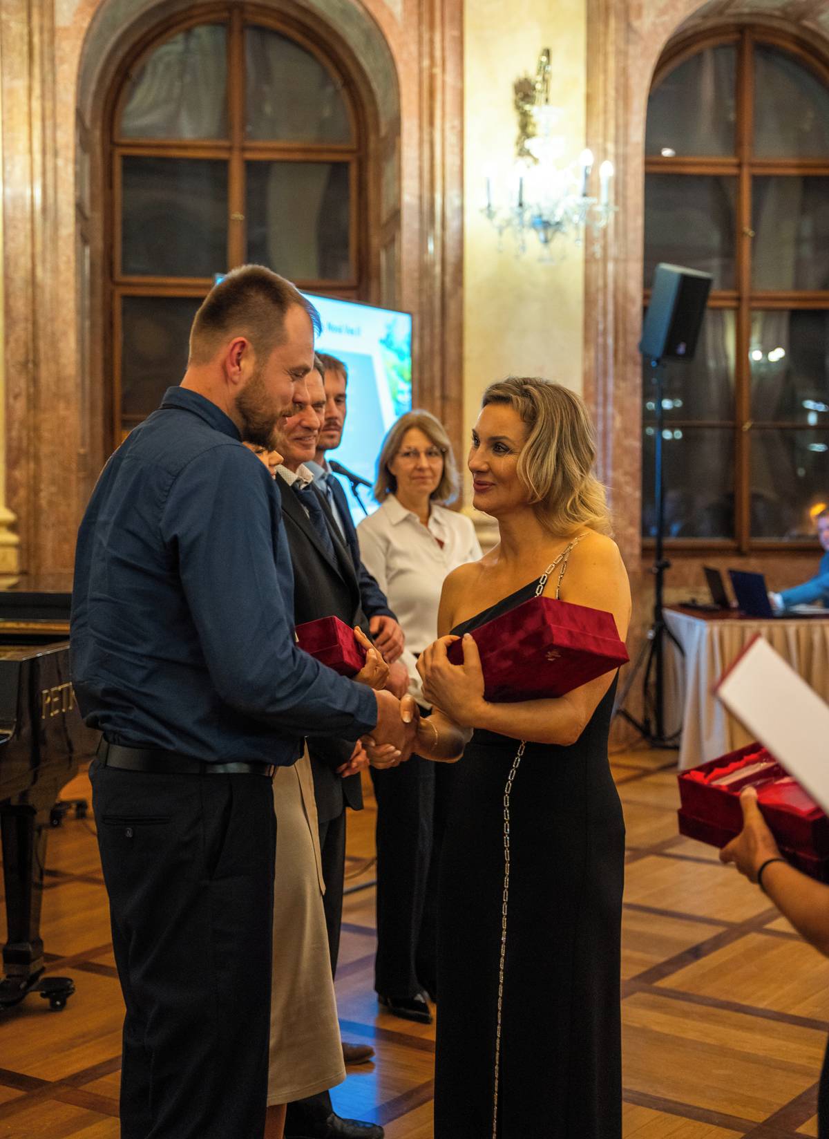 V 18. ročníku soutěže Žít krajinou, kterou pořádá Státní pozemkový úřad a Českomoravská komora pro pozemkové úpravy, obdržela Obec Rostoklaty hned dvě ceny. Nejprve to bylo 1. místo v kategorii Opatření k ochraně a tvorbě životního prostředí. Na konci slavnostního večera, který se konal v sídle Senátu Parlamentu v Rytířském sále Valdštejnského paláce, se vyhlašovala ještě Cena Státního pozemkového úřadu. A tu obdržel, společně s projektem retenční nádrže v obci Lechotice, opět projekt ÚSES z Nové Vsi II. Hodnotící komise se totiž nedokázala rozhodnout pro jeden projekt, a tak výjimečně ocenili oba dva projekty. Co to je vlastně ten ÚSES, který nás dostal do Senátu, zaujal ministra zemědělství natolik, že se přijel osobně podívat? Územní Systémy Ekologické Stability jsou opatření v krajině používané k ochraně přírody a územním plánování k zachování nebo obnově ekologicky stabilní krajiny. Tedy je to návrat remízků, větrolamů či vodních prvků do krajiny, která ztrácí svojí stabilitu v důsledku klimatické změny a intenzivního zemědělského hospodaření. Biocentra jsou mezi sebou propojena biokoridory a společně tak tvoří funkční ekologickou síť. Konkrétní projekt z naší obce je příkladem, jak by to mělo fungovat. Vše začalo Komplexní pozemkovou úpravou (KPÚ), která byla dokončena v roce 2005. Ta zcelila rozdrobené pozemky jednotlivých vlastníků, vyčlenila pozemky pro přístupové cesty v krajině a právě i ty pozemky, na kterých by se jednou mohly realizovat ÚSESy. V roce 2011 byla vybudována polní cesta P 6 za 7.591.123 Kč, hrazená převážně z Programu rozvoje venkova. Ta začíná na silnici Tismice - Nová Ves II a vede v délce cca 1,5 km podél produkčního  sadu a toku Štolmířského potoka. V roce 2013 byl na 15 m širokém pruhu při levém břehu Štolmířského potoka vysázen Biokoridor s počtem 1800 ks sazenic stromů a 5344 ks keřů, náklad 1.539.416 Kč. Posledním dílkem skládanky byla realizace Biocentra BC 6 v roce 2019. To má plochu 1,44 ha a zahrnuje květovou louku se solitérními stromy, lesnickou výsadbu lipovo bukových doubrav, vyhloubenou tůňku, plazník, kamennou rovnaninu a zemní hrázku. Náklady byly 1.905.681 Kč. Veškeré výše uvedené částky nebyly hrazeny z obecního rozpočtu, tedy peníze za stromky nechybí na asfalt silnice před vaším domem. Diplomy a sošky z broušeného skla jsem měl sice tu čest převzít z rukou ministra zemědělství pana Marka Výborného já, ale moje zásluha to rozhodně není. Role obce zde byla taková, že poskytla pozemky pro realizaci, účastnila se kontrolních dnů a zavázala se k následné péči. Spolu s obcí byla oceněna pobočka SPÚ v Kolíně, projekční kancelář GAP Pardubice a dodavatelská firma Školky Montano. Skromně tedy prohlašuji, že toto ocenění není pro mě, ale pro obec Rostoklaty, zásluhy má tedy i předchozí vedení obce. Na partu ukrajinců, kteří to tam v zimě, dešti a blátě sázeli, v horkém létě zalévali, na ty si dnes už nikdo nevzpomene. Skromně jsem tedy ze sebe oklepal cizí peří, kterým bych se nerad chlubil. Namyšleně ale říkám, že je to možná karma, že ocenění jsem si rád převzal, protože v katastrálních území obou částí naší obce jsem zorganizoval několik dalších výsadeb a stabilizačních prvků. A říkám, že pouze zorganizoval, protože práci při odvedli mnozí z Vás při komunitních výsadbách, dále se účastnili kamarádi ze skauta, kolegové myslivci ze spolku, zaměstnanci obce a dobrovolníci z nadace Sázíme stromy.