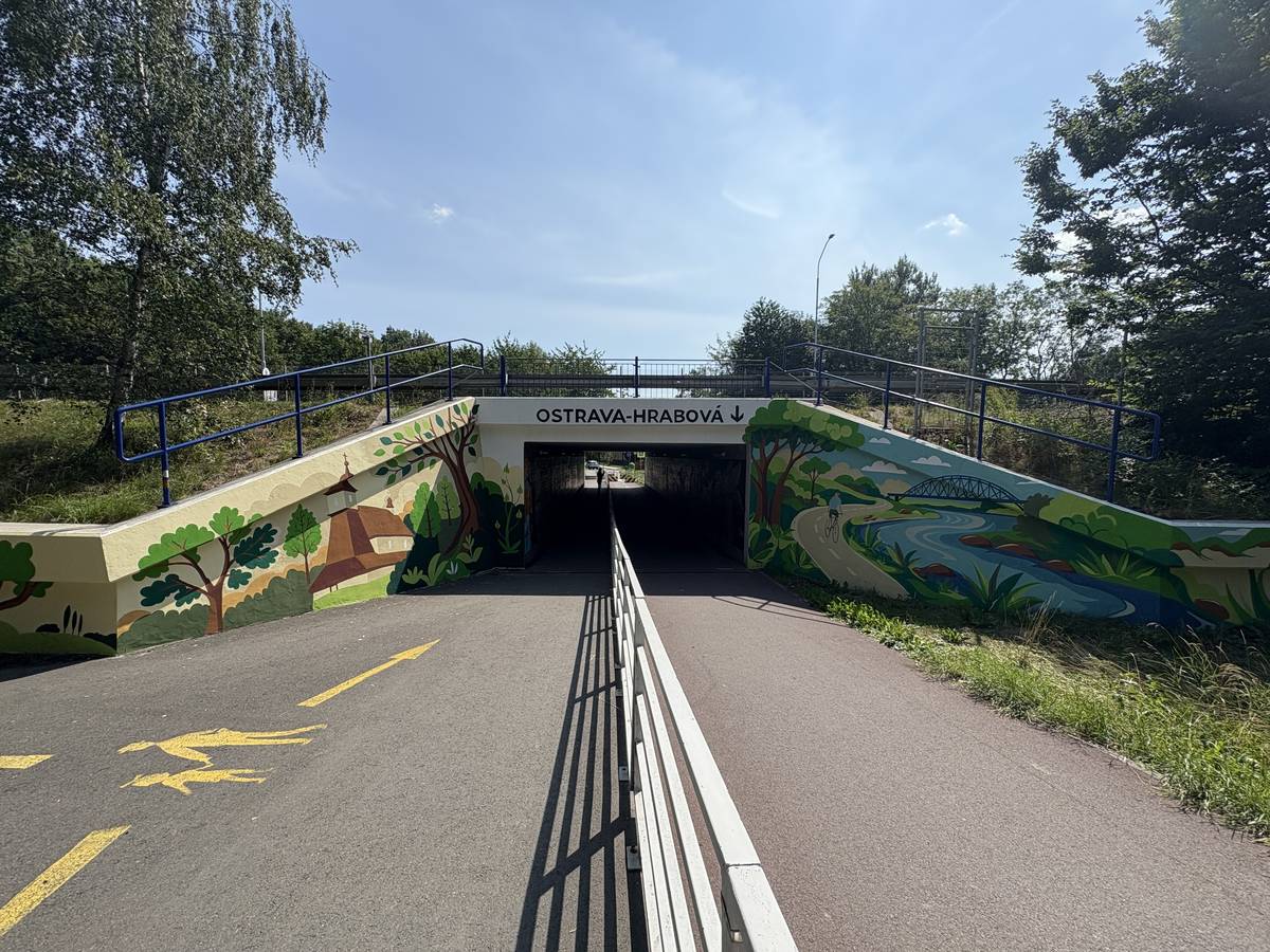 Novou podobu získalo průčelí vstupu do podchodu mezi Hrabovou a Hrabůvkou pod frekventovanou ostravskou tepnou Místecká, nedaleko autobusové zastávky Benzina. Na původně šedých stěnách poničených graffiti vzniklo další umělecké dílo, které tematicky navazuje na výmalbu vnitřních stěn podchodu. „Tu jsme realizovali v roce 2024. Z důvodu poškození sprejery a vandaly jsme nyní přistoupili k úpravě průčelí,“ říká místostarosta Otakar Šimík. Motiv ve směru na Hrabovou zobrazuje známý místní kostel, pravou stranu zdobí cyklostezka u Ostravice. Ve směru do Hrabůvky je na levé straně zachycen těžební průmysl Ostravy, pravou část pak doplňuje koláž tramvají.