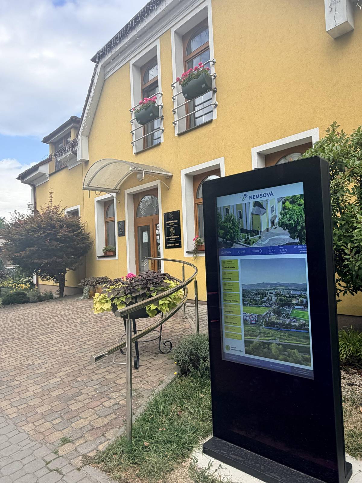 📌Pri mestskom úrade v Nemšovej je pre obyvateľov a návštevníkov mesta k dispozícii nová digitálna úradná tabuľa, ktorá prispeje k lepšej informovanosti občanov a poskytne jednoduchší prístup k aktualitám a dianiu v našom meste...  🔍Okrem oficiálnych dokumentov a noviniek si môžete:  🗞️prelistovať Nemšovského spravodajcu, 📢prečítať oznamy z mestského rozhlasu, 📸pozrieť fotogalériu z mestských podujatí, 👀či nahliadnuť do mapového portálu...  🙌Súčasťou je aj prepojenie na webovú stránku mesta a aplikáciu MUNIPOLIS...
