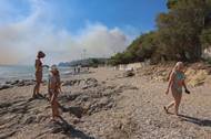 Lidé na pláži pozorují kouř stoupající z lesního požáru poblíž vesnice Plomari na ostrově Lesbos